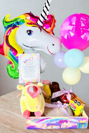 Colorful unicorn foil balloon with rainbow mane beside a pink balloon and pastel balloons at a birthday setup on a wooden floor.